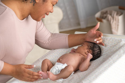 A mother smiles down on her diapered baby on a changing table